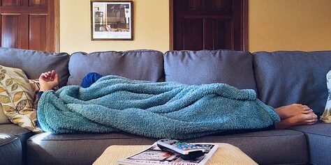 Person with chronic fatigue hiding under a blanket